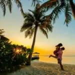 Um homem e uma mulher estão em pé na praia ao pôr do sol.
