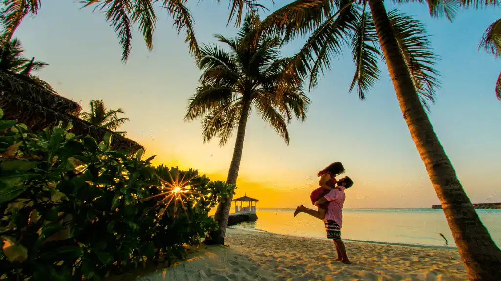 Um homem e uma mulher estão em pé na praia ao pôr do sol.