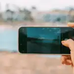 Mão segurando um smartphone tirando uma foto da paisagem do mar.