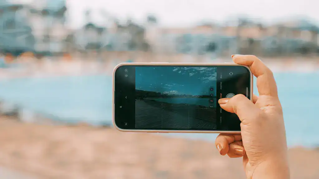 Mão segurando um smartphone tirando uma foto da paisagem do mar.