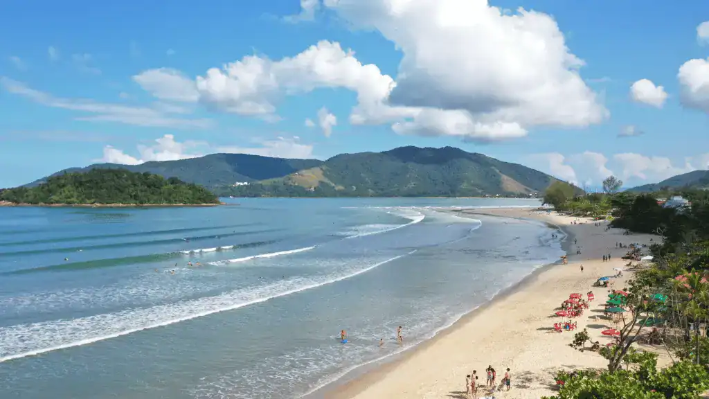 Vista panorâmica da Praia das Toninhas em Ubatuba com mar calmo, faixa de areia clara e famílias aproveitando o dia de sol, ideal para crianças.